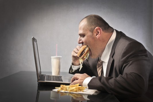 Mann isst Hamburger im Büro